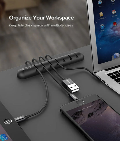Desk setup with a cable organizer, laptop, and smartphone on a wooden surface.