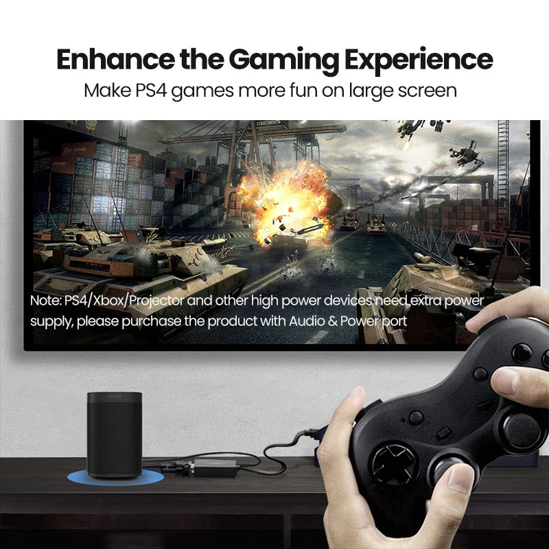 A gaming setup scene showing a black cylindrical audio device on a desk, a black game controller in hands, and a large wall-mounted screen displaying a war scene. Text at the top reads 'Enhance the Gaming Experience' and 'Make PS4 games more fun on large screen,' with a note about PS4/Xbox/Projector power requirements.