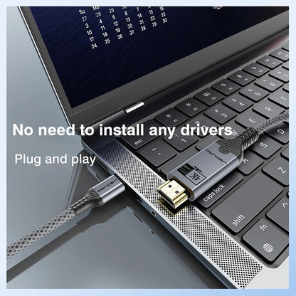 A close-up of a laptop keyboard with a braided USB cable plugged into the side port. The cable has a silver connector and a black-and-silver adapter labeled 'USB 3.
