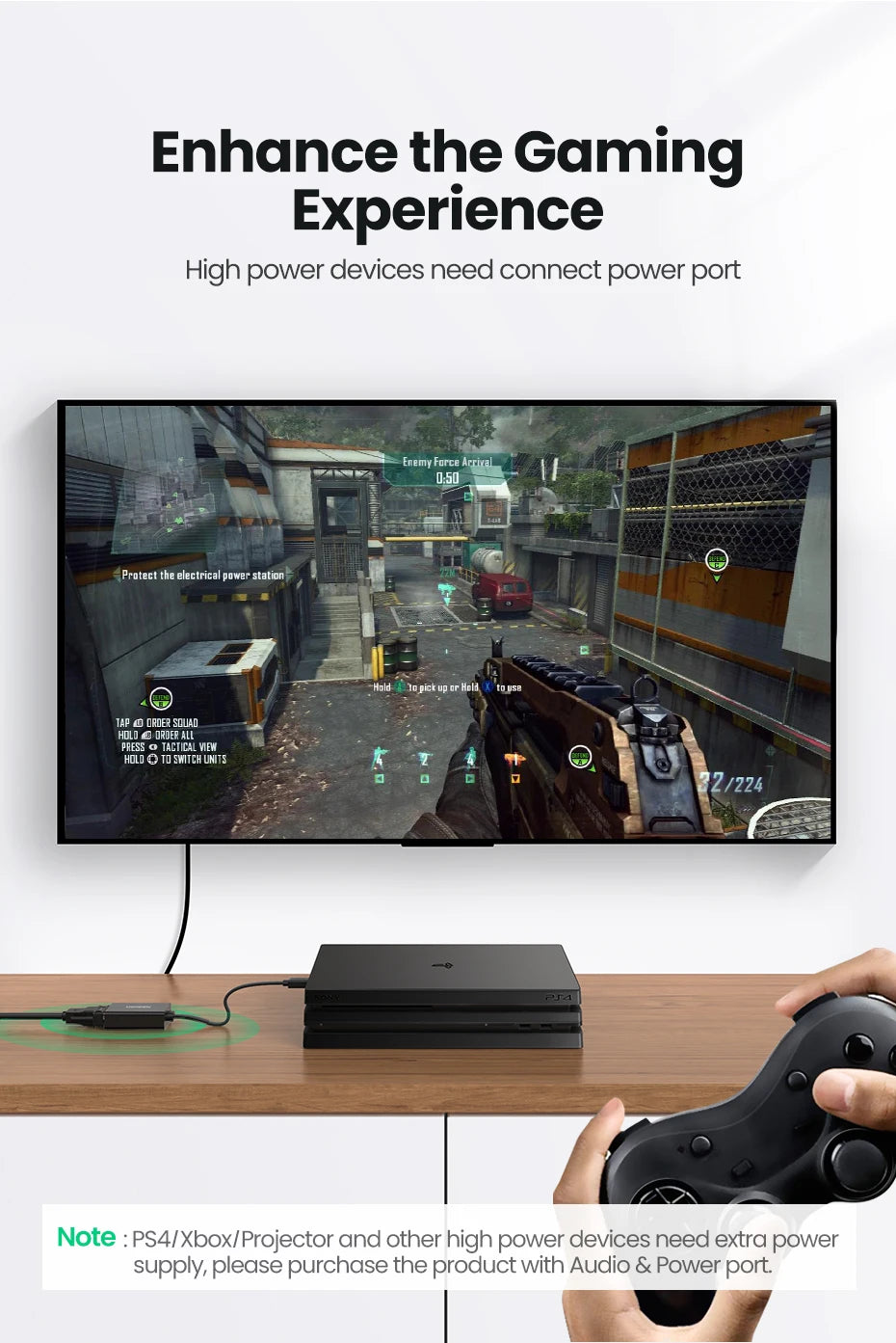 A gaming setup scene showing a large wall-mounted screen displaying a first-person shooter game, with a black PlayStation-style console on a wooden surface below and a hand holding a wired controller. Text at the top reads 'Enhance the Gaming Experience' and a note at the bottom mentions PS4/Xbox/Projector and extra power supply.