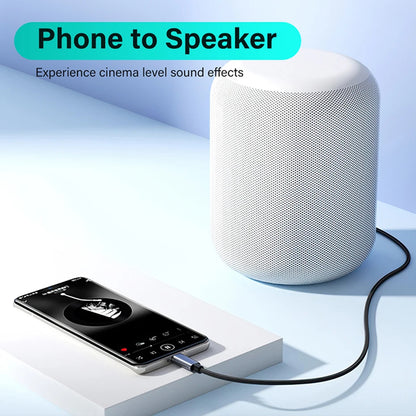 A white cylindrical speaker connected to a smartphone via a black cable, shown on a clean light blue studio background with promotional text reading 'Phone to Speaker'.