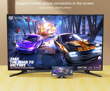 A large flat-screen TV on a light wood surface against a beige wall, showing a racing game scene with two cars and on-screen PUBG and Dodge branding. A small phone is placed in front of the TV to demonstrate mobile connection.