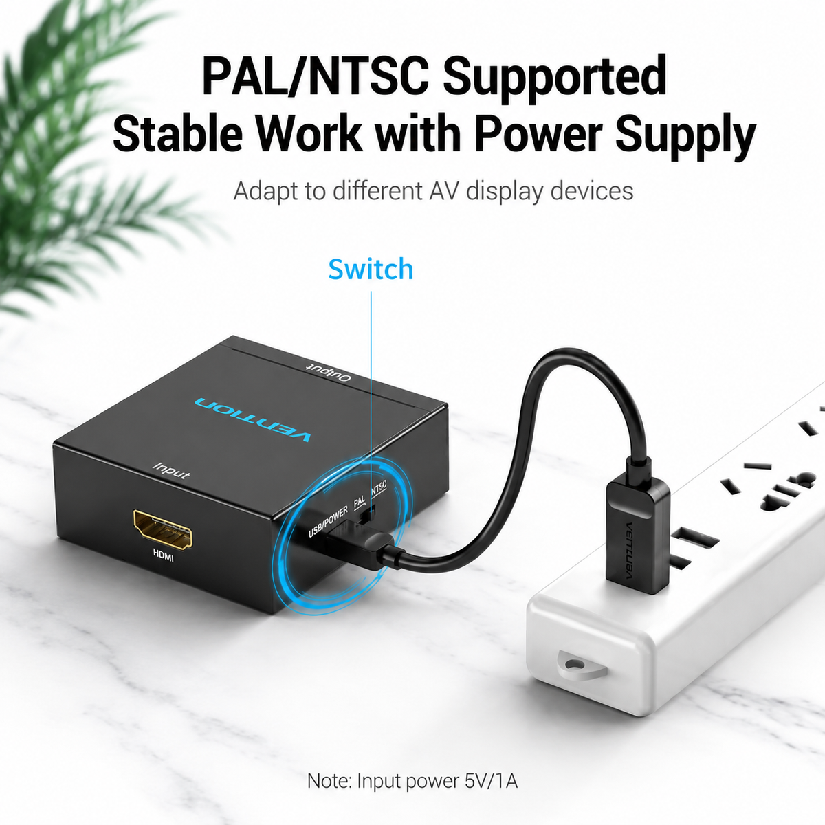 A black Vition HDMI adapter shown plugged into a white power strip on a light marble surface, with marketing text above and a blue callout pointing to the switch. The adapter is the product being sold; the power strip and plant leaves are contextual props.