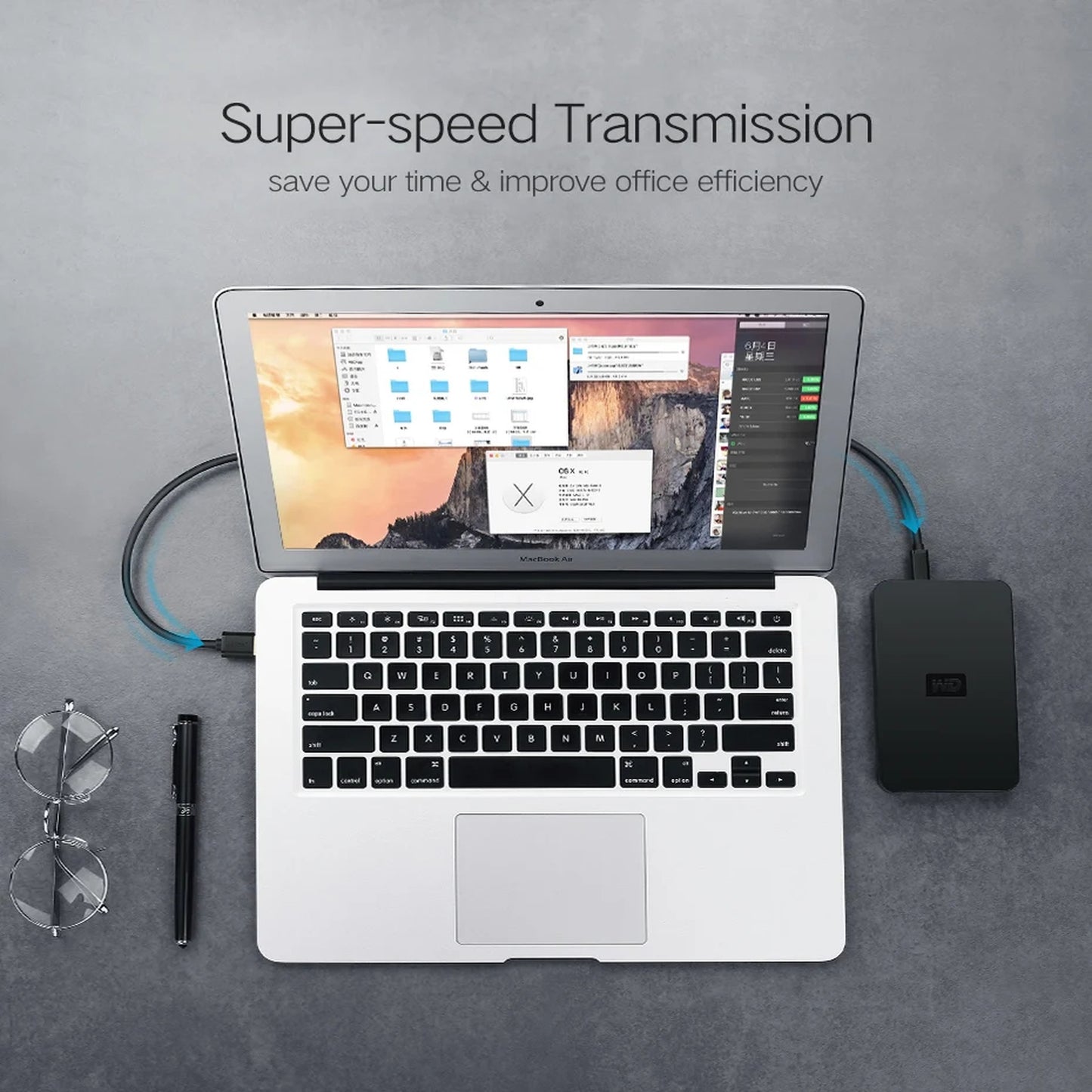 A silver laptop connected to a black external drive or power unit with blue cables, arranged on a gray surface with glasses, a pen, and promotional text reading 'Super-speed Transmission'.