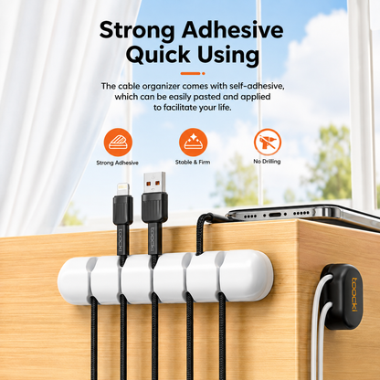 White adhesive cable organizer clips mounted on a wooden desk, holding black cables with a smartphone resting on top. Text at the top reads 'Strong Adhesive Quick Using' with feature icons for strong adhesive, stable and firm, and no drilling.