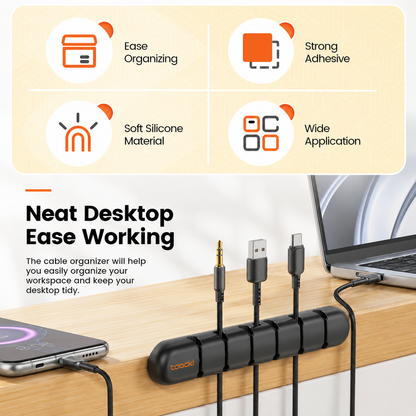 A black cable organizer dock shown on a wooden desk with connected cables, a laptop, and a phone. The top portion includes feature callouts: Easy Organizing, Strong Adhesive, Soft Silicone Material, and Wide Application.